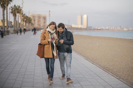 Couple sharing a message on the smart phone, They are walking in the beach in Barcelona on a winter day.
