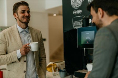 Smiling male colleagues making a coffee next to the coffee machine while standing in the cafeteria the office.