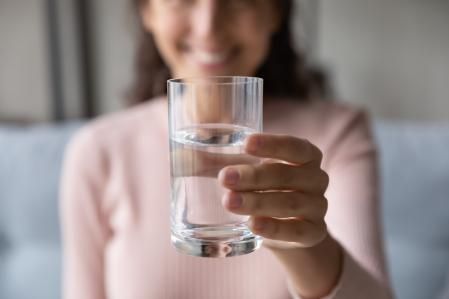 Primer plano de una mujer feliz que extiende la mano con un vaso de agua fresca
