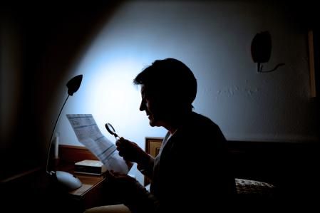 Una mujer mayor mira con lupa la letra pequeña de la factura de la luz