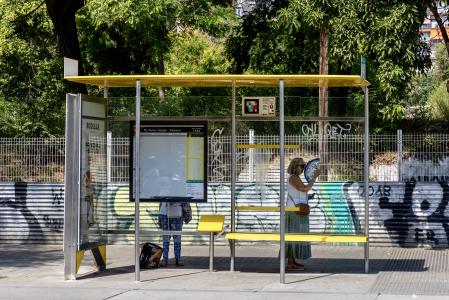 Unas viajeras se refugian del sol buscando la sombra tras la marquesina del autobús