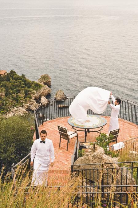 Dos camareros preparan la mesa para la cena en la terraza frente al mar del Grand Hotel San Pietro en Taormina.
