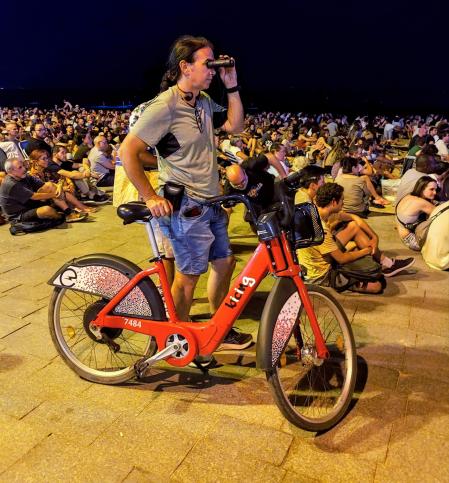 Ciclista siguiendo el concierto en la playa con unos prismáticos.