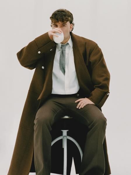 Quevedo a encontrado el lujo en poder ser feliz. Corbata tejida de punto gris. Abrigo utilitario de botonadura sencilla tipo kimono. Pantalón de tweed marrón con cordón. Cortesía de Louis Vuitton