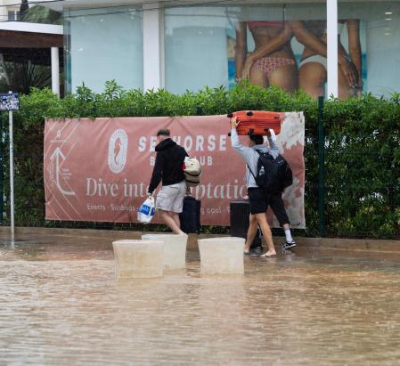 Unos turistas caminan por una calle de Eivissa totalmente anegada.&nbsp; (Photo by Vicent MARI / AFP)