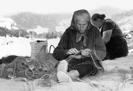 Mujer cosiendo redes en una imagen antigua.