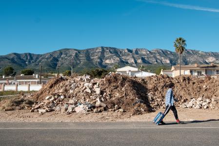 Un vecino se marcha de viaje frente a los escombros, barro y restos del último aguacero del 12-O&nbsp;