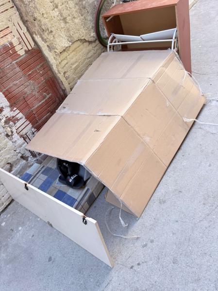 Una persona duerme en el interior de una caja de cartón dispuesta en el pasaje, con los pies asomando ligeramente