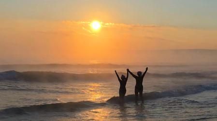 Dos mujeres reciben el primer amanecer del año con los brazos en alto.