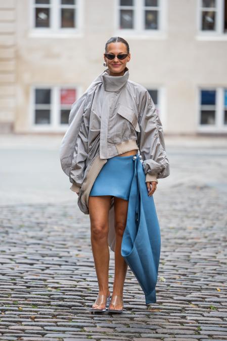 Tine Van Cauwenberghe lleva una minifalda asimétrica azul y una chaqueta corta gris en el desfile de Freya Dalsjø durante la Semana de la Moda de Copenhague.