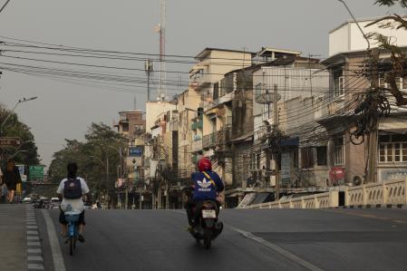 Una motocicleta circula por Samsen Rd, flanqueada por edificios antiguos y marañas de cables