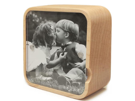Caja de música de madera clara con marco para foto, mostrando una imagen en blanco y negro de dos niños besándose.