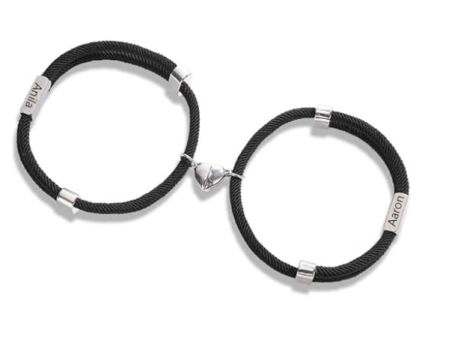 et de pulseras negras para pareja con corazón magnético central y nombres grabados.