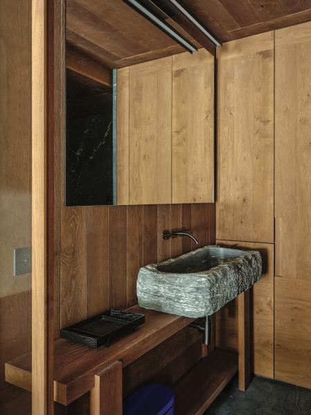 En el baño, sobre la encimera, que evoca una mesa de carpintero, lavamanos de piedra realizado a partir de un bloque vaciado con acabado rústico