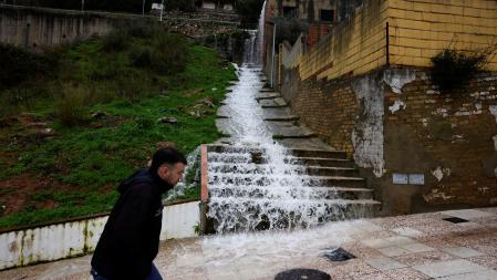 Un hombre camina mientras el agua fluye a borbotones por las escaleras en una calle de Grazalema