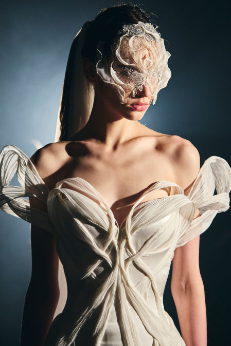 'Lumare', vestido nupcial - Cuerdas de marfil plisadas a mano emanan del corpiño. Se drapean y se entrelazan en pliegues. Velando el rostro, la seda esculpida se funde con encaje bordado en plata&nbsp;