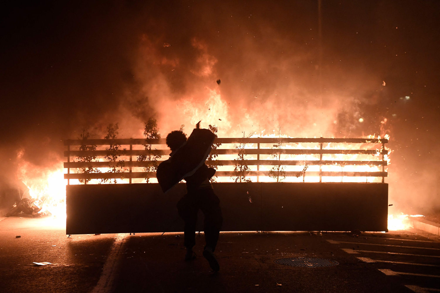 A protester throws a stone into flames during clashes with Catalan regional forces Mossos d'Esquadra after a demonstration against the arrest of Spanish rapper Pablo Hasel in Barcelona on February 16, 2021. - Spanish police stormed a university to arrest the rapper barricaded inside after being sentenced to nine months' jail over tweets attacking the monarchy and the police in a case denounced as an attack on freedom of speech. (Photo by Josep LAGO / AFP)