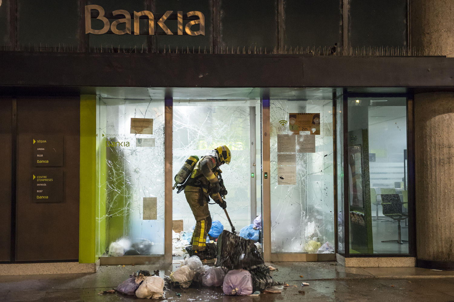 Un bombero apaga un incendio en una sucursal de Bankia tras la marcha en apoyo al rapero Pablo Hasel que ha degenerado en disturbios en Girona, Cataluña (España), a 16 de febrero de 2021. El rapero Pablo Hasel ha ingresado la mañana de este martes en el centro penitenciario de Ponent, en Lleida, tras ser arrestado por los Mossos d'Esquadra. Está condenado por la Audiencia Nacional a dos años, cuatro meses y quince días de cárcel por los delitos de enaltecimiento del terrorismo e injurias a la corona. Hasel se había encerrado en el edificio del rectorado de la Universitat de Lleida (UdL) este lunes junto a miembros de su grupo de apoyo para impedir el arresto. 16 FEBRERO 2021 Glòria Sánchez / Europa Press 16/02/2021