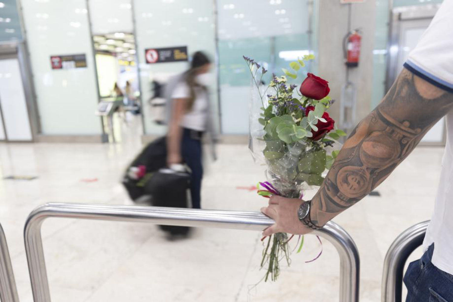 Un hombre espera a su pareja con una rosa en el aeropuerto de Barajas