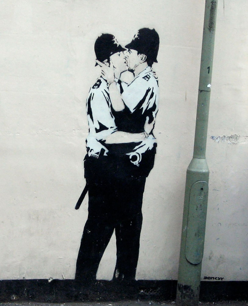 Kissing Coppers - Banksy. Los dos policías están pintados en blanco y negro. Ambos individuos aparecen con el uniforme completo, con evidentes esposas y una porra en sus respectivos cinturones. Esta representación de la intimidad entre personas del mismo sexo es una característica común del arte que se remonta al siglo XVI en el techo de la Sixtina de Miguel Ángel. Otro elemento significativo de Kissing Coppers es su ubicación estratégica porque se realizó en Brighton, que es un barrio muy animado y al que se ha denominado la capital LGBT del Reino Unido.