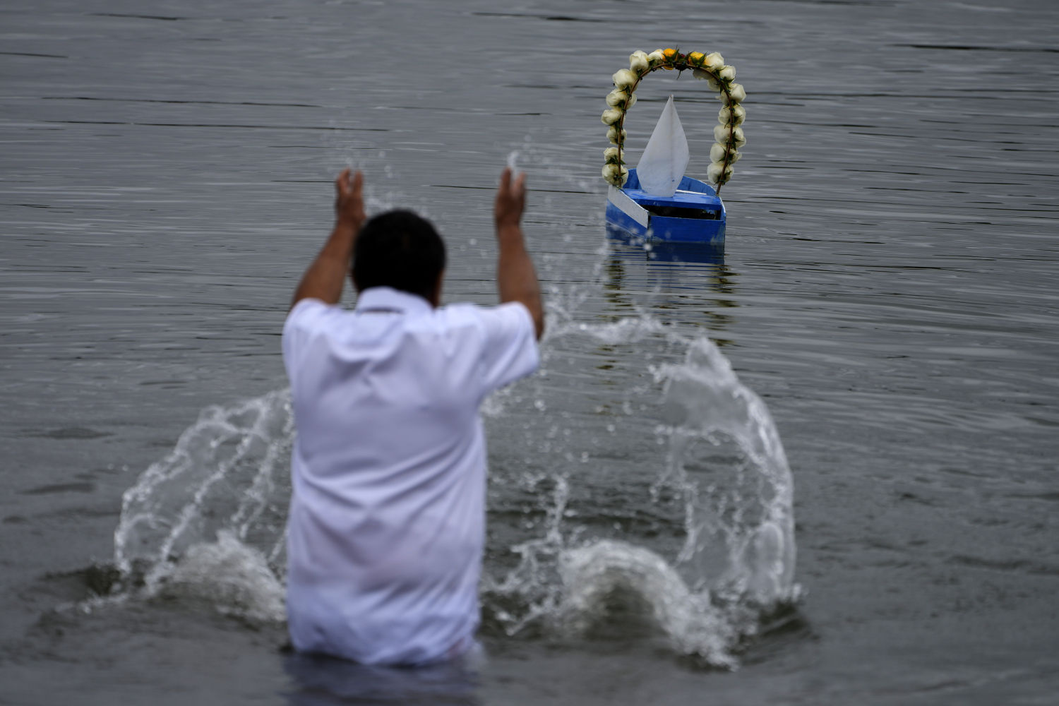 Un clérigo de Yemanja arroja agua hacia un pequeño bote con ofrendas para Yemanja, una deidad celebrada por la religión africana yoruba, en un lago en el centro de Brasilia, Brasil, en la víspera de Año Nuevo. A medida que el año termina, los religiosos brasileños celebran a Yemanja, diosa del mar, ofreciendo flores y lanzando botes grandes y pequeños al agua a cambio de bendiciones para el próximo año.