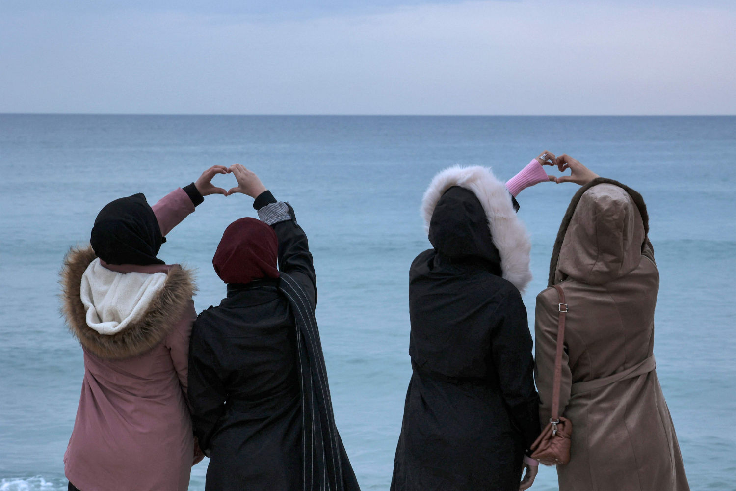 Cuatro mujeres juntan sus manos para crear gestos en forma de corazón a lo largo de una playa en la ciudad de Gaza antes del último atardecer del año.
