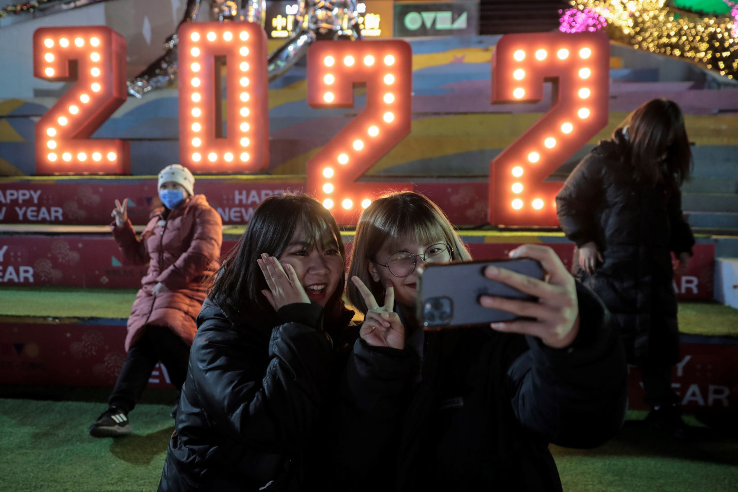 Dos chicas posan para un selfie frente a una decoración de 2022 afuera de un centro comercial para celebrar el próximo año nuevo 2022 en Beijing, China.
