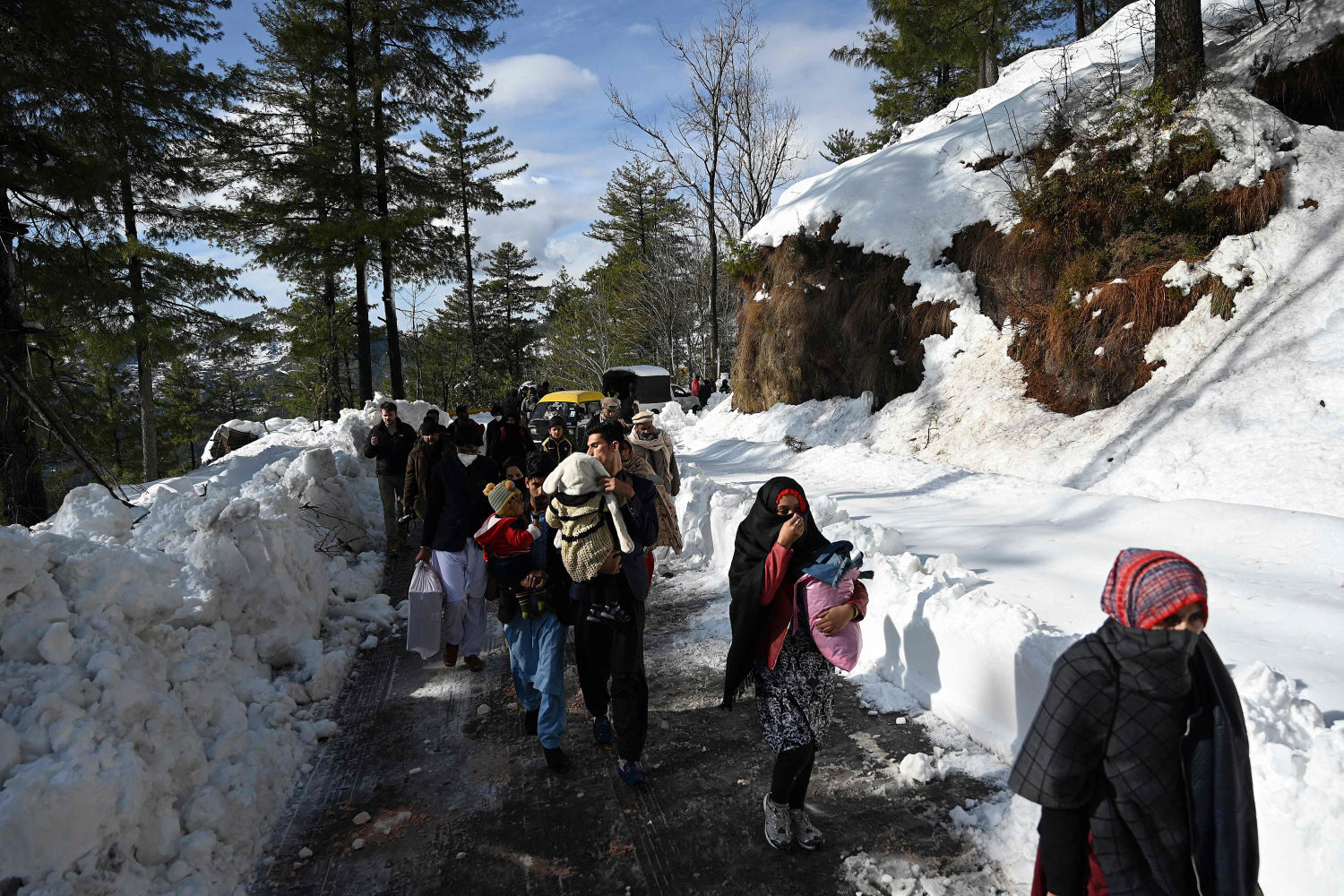 Los turistas caminan a lo largo de un camino cubierto de nieve luego de una tormenta de nieve que comenzó el 7 de enero y que dejó a los visitantes atrapados en vehículos a lo largo de los caminos hacia la ciudad turística de Murree, a unos 70 km al noreste de Islamabad (Pakistan) el 9 de enero de 2022.
