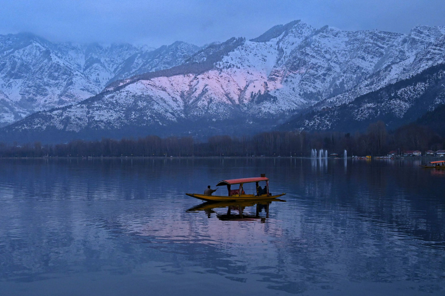 La gente disfruta de un paseo en bote con montañas cubiertas de nieve de fondo en el lago Dal en Srinagar (India) el 11 de enero de 2022.