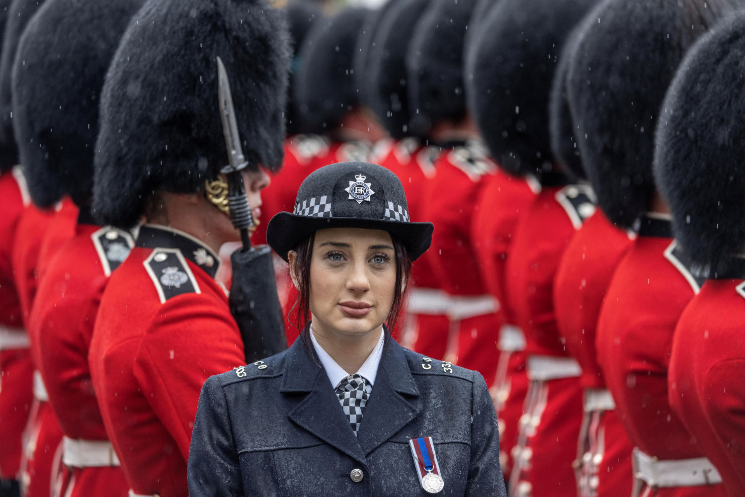 Una agente de policía ante guardias ceremoniales esperan bajo la lluvia mientras el rey Carlos y la reina Camila abandonan la Abadía de Westminster