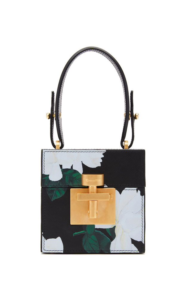 Un estampado floral de gardenias y herrajes dorados adornan la particular textura 'saffiano' de la piel de becerro del bolso de mano Alibi Cube. El interior de forro de gamuza de este cofre de los tesoros está tan cuidado como el exterior e incluye un espejo