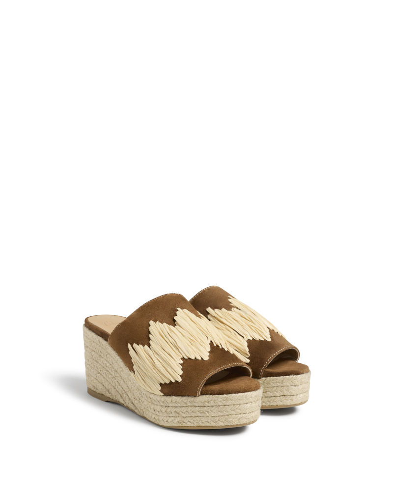 Confeccionadas a mano en serraje y rafia, las nuevas 'mules' con cuña de Castañer sorprenden con un original en tramado de color crema en la parte frontal que contrasta con la piel marrón de la base