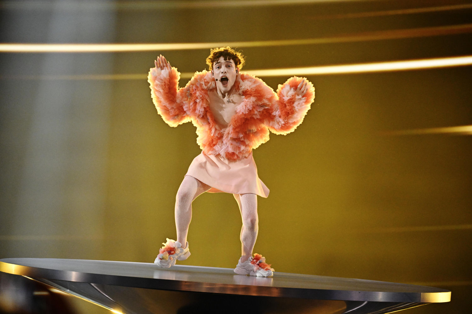 Nemo, representando a Suiza, con una chaqueta de pelo naranja a juego con una mini falda y unas sneakers con pompones de pelo