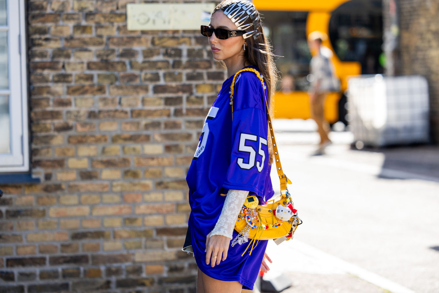 Una invitada viste un bolso Balenciaga amarillo con accesorios, una camiseta de fútbol, ​​pinzas para el cabello y pantalones cortos en las afueras de Joao Maraschin durante el segundo día de la Semana de la Moda de Copenhague (CPHFW) SS25 el 6 de agosto de 2024 en Copenhague, Dinamarca.