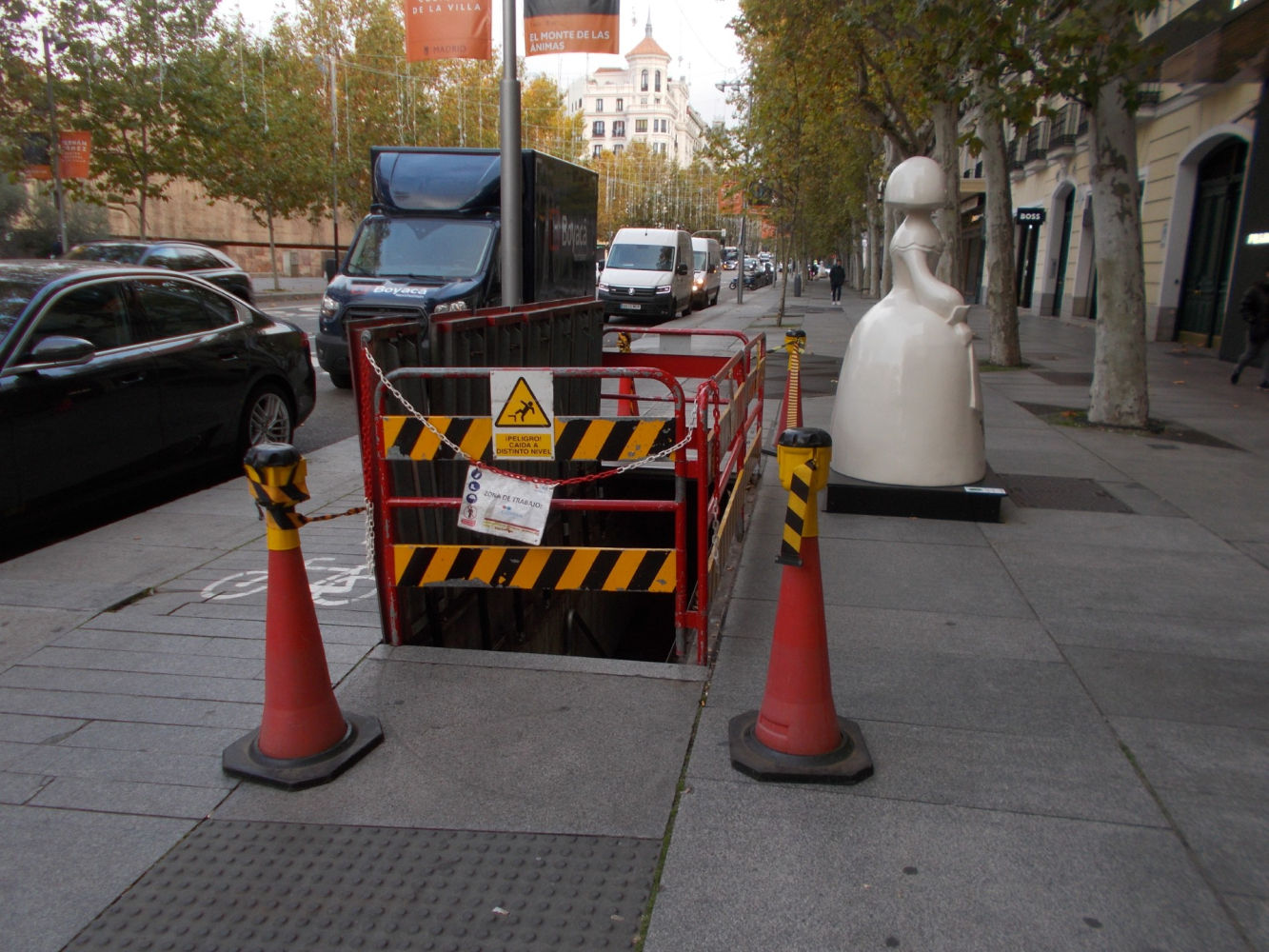 En una céntrica calle madrileña, una Menina, impertérrita, permanece junto a unas compuertas entreabiertas en la acera con un cartel de 