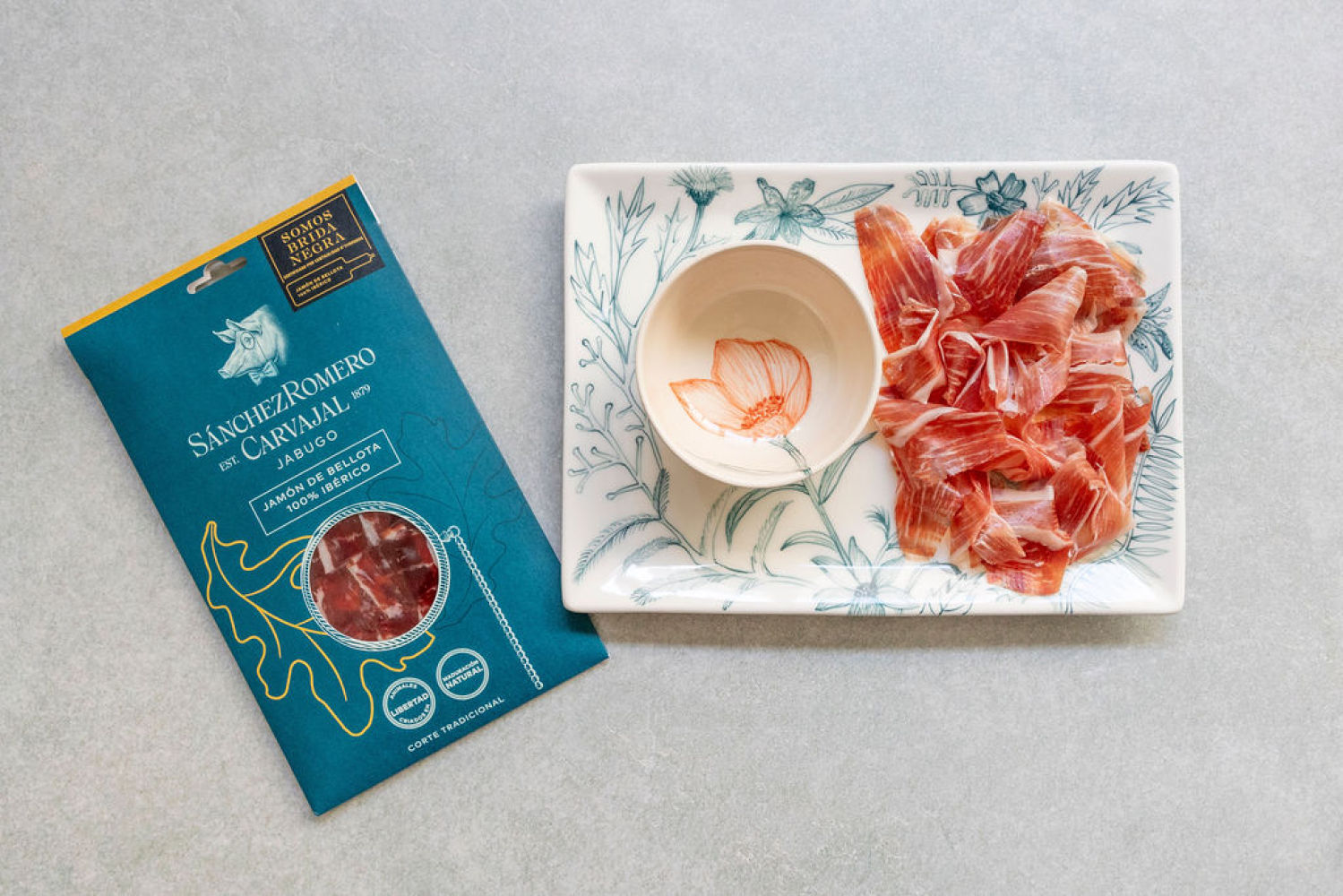 Este pack especial para las fiestas  incluye un sobre de Jamón de Bellota 100% Ibérico Sánchez Romero Carvajal y dos piezas de cerámica pintadas a mano por la artista Nuria Blanco  i
