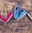 Five pairs of various running shoes hang on a nail on a wooden fence background