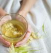 A cup of herbal tea (lime blossom/ linden tea) photographed on a cozy beige blanket with herbal flowers in the background.