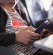 Close-up of a young girl sitting in airplane and using smartphone with in-ear headphones