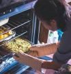 Una mujer cocina varias comidas en un horno
