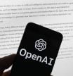 El logotipo de OpenAI en un teléfono móvil frente a una pantalla de computadora que muestra el resultado de ChatGPT.