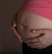 Young pregnant between 30 and 35 years old woman touches her belly. Dramatic light. Closeup