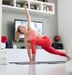 Attractive sporty woman working out at home, doing pilates exercise in front of television in her living room. Social distancing. Stay healthy and stay at home during corona virus pandemic.