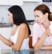 Young girl using her smartphone at kitchen table, her mother are near her