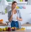 Shot of pretty young woman eating yogurt while standing in the kitchen at home.