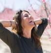 Beautiful middle age woman in the middle of pink peach flowers and trees smiling cheerful with open arms enjoying sunbathe on sunny day (Beautiful middle age woman in the middle of pink peach flowers and trees smiling cheerful with open arms enjoying