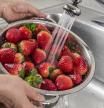 Una mujer lavando fresas bajo el grifo