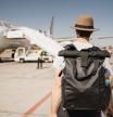 white young man with hat and suitcase walking through the airport near the takeoff runway