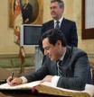 Moreno Bonilla escribe en el libro de honor del Ayuntamiento de Sevilla con Juan Espadas al fondo (Junta de Andalucía)