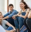 Group of happy young friends sitting in college campus and talking. Cheerful group of  smiling girls and guys feeling relaxed after university exam. Excited millenials laughing and having fun outdoor.